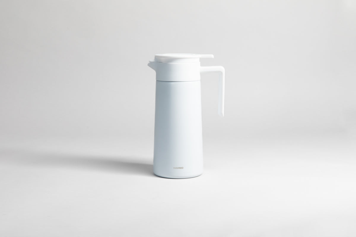 White cylindrical pot with an white polypropylene spout, handle and lid. Set on a light gray background