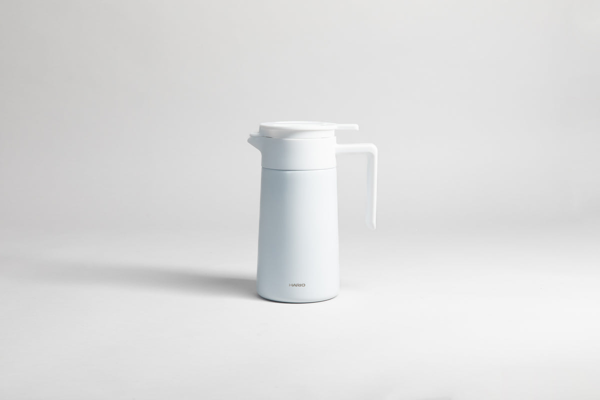 White cylindrical pot with an white polypropylene spout, handle and lid. Set on a light gray background.