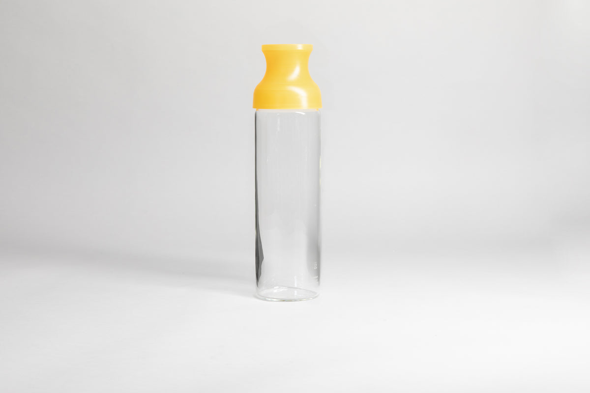 Cylindrical glass bottle with a clear yellow silicone wide mouth spout. set on a white background