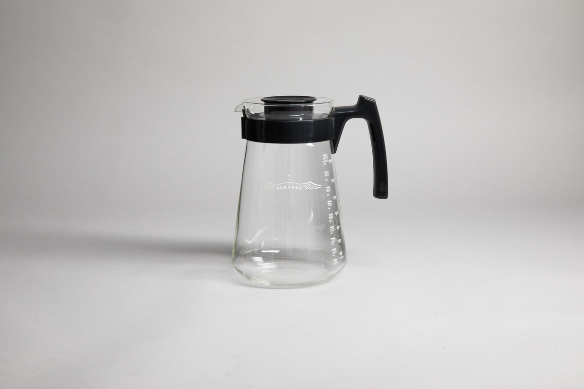 Glass coffee server with white text and level markings with black hard plastic handle and lid on a light grey background.