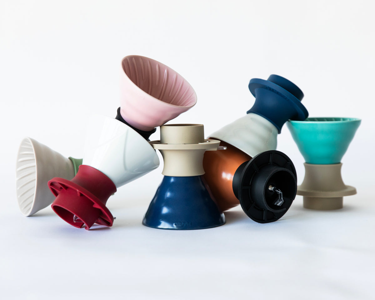 A colorful assortment of V60 ceramic cone coffee drippers with various silicone bases, arranged in a pile on a white background.