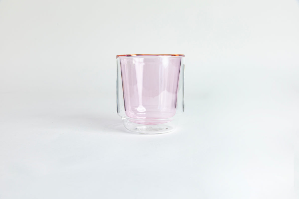 A clear double-walled glass with pink colored interior cup. set on a white background