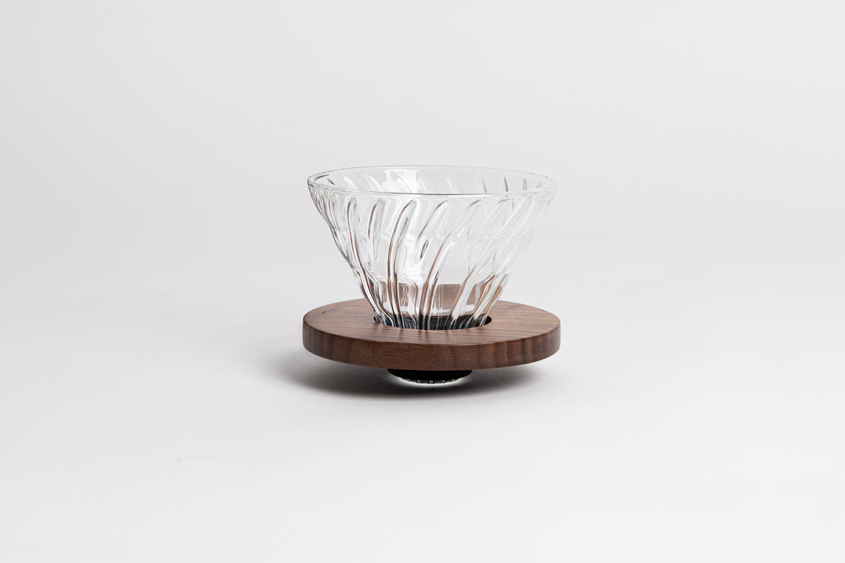 Clear all glass cone shaped coffee dripper with ribs, sitting in a round walnut wood base.