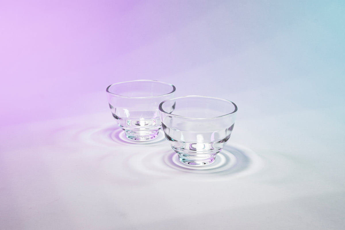 Two matching short glass tea cups with beehive shape against purple to blue gradient background.