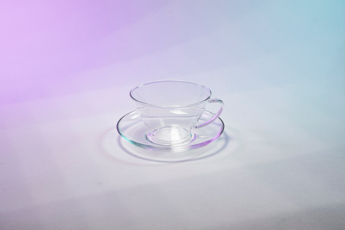 Tapered small glass cup with full glass handle sitting in a matching glass saucer.