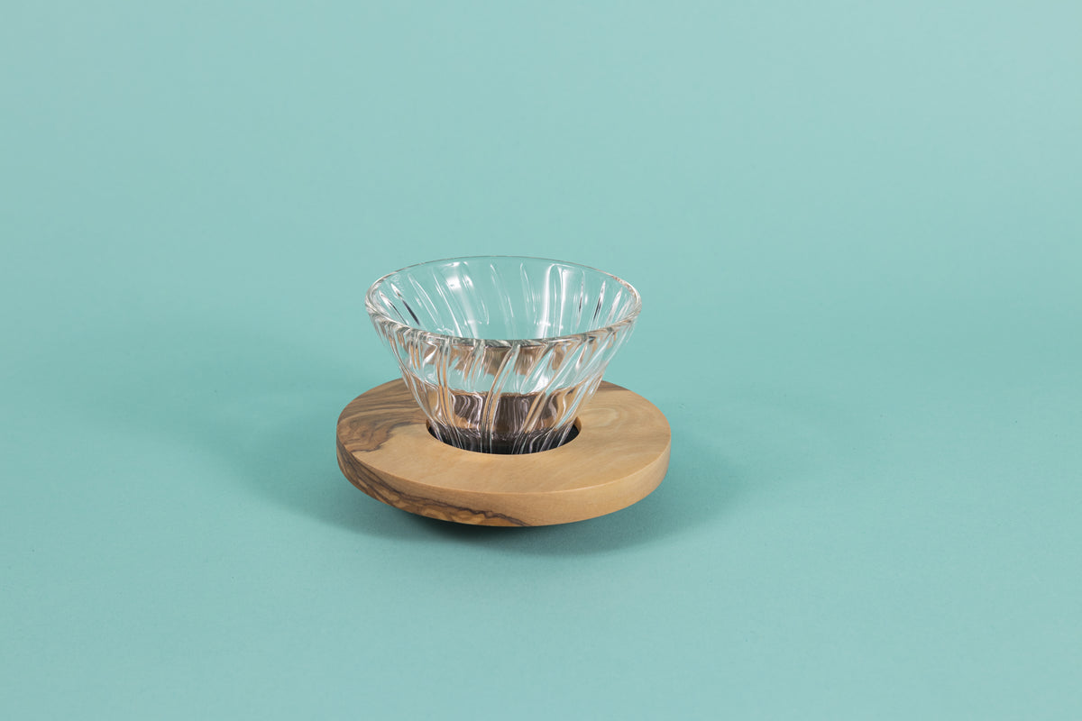 Clear all glass cone shaped coffee dripper with ribs, sitting in a round olive wood base.