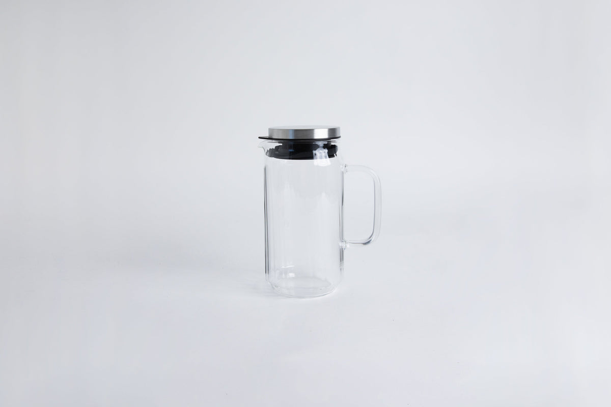 Clear glass pitcher with glass handle with metal lid and black gasket. Set on a white background