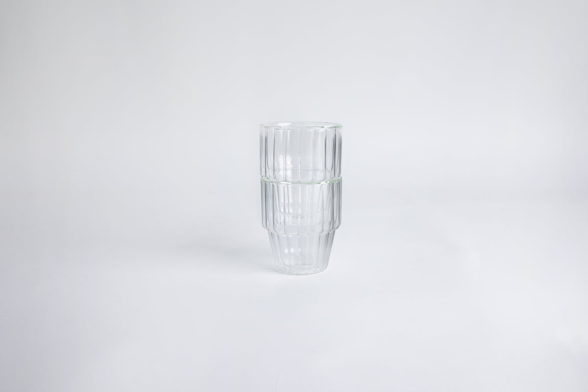 2 ribbed glass cups stacked on top of each other. set on a white background.