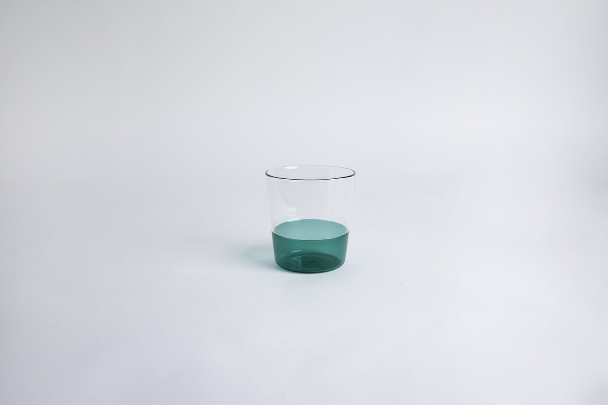 Dual colored clear glass cup, top  half is clear and second half colored teal green set on a white background