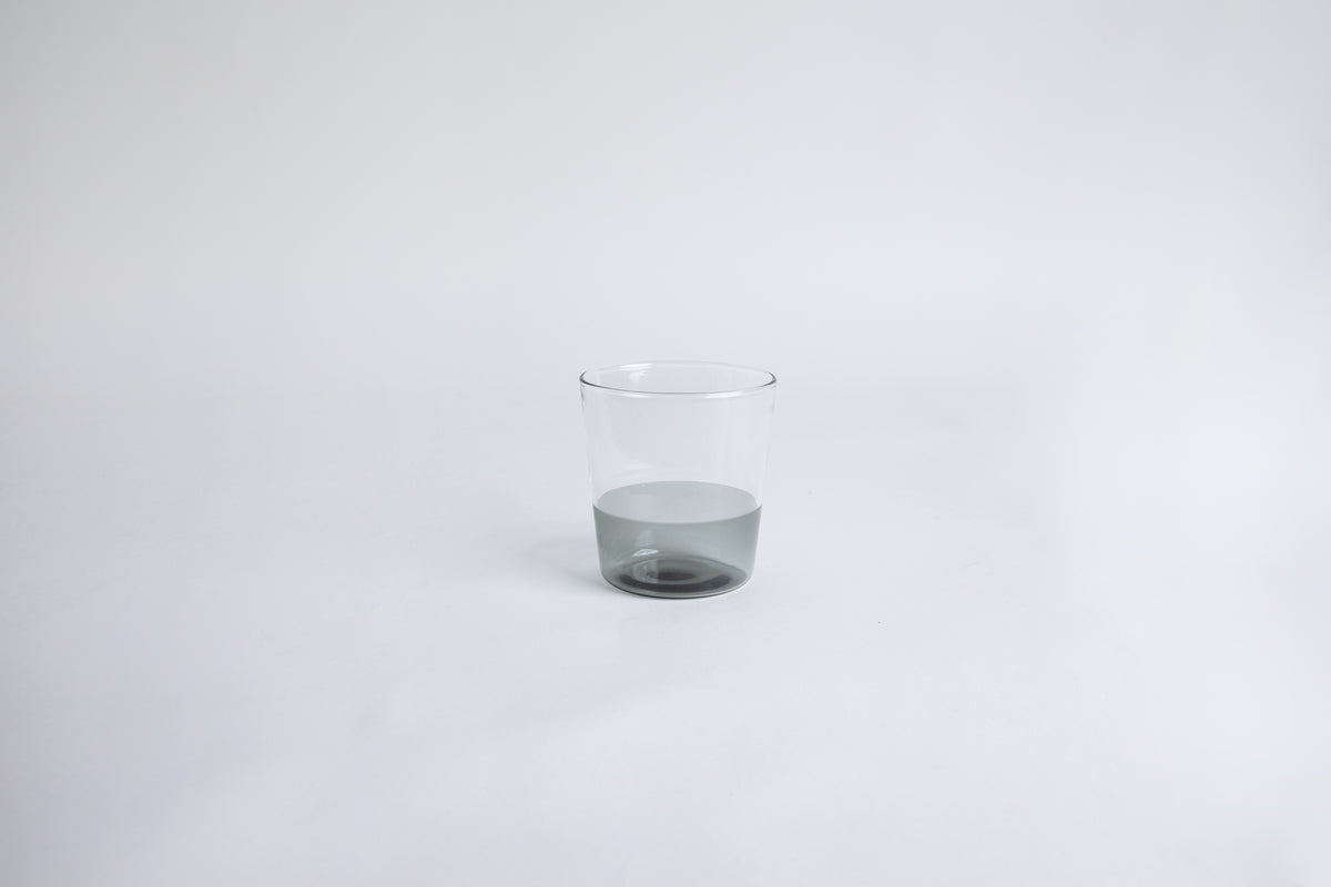 Dual colored clear glass cup, top  half is clear and second half colored gray set on a white background