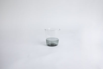 Dual colored clear glass cup, top  half is clear and second half colored gray set on a white background