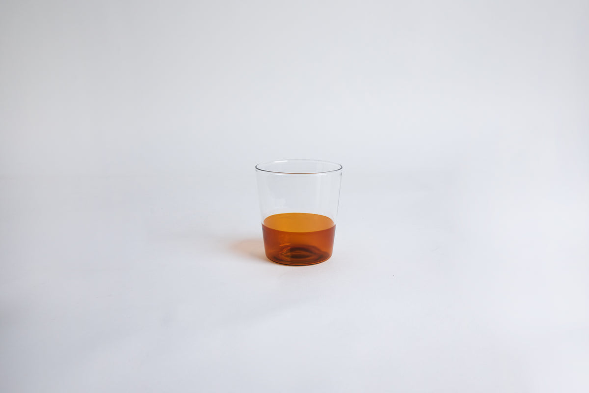 Dual colored clear glass cup, top  half is clear and second half colored amber set on a white background