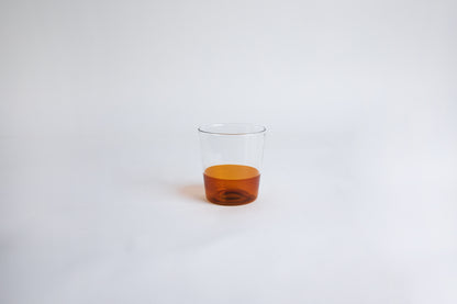 Dual colored clear glass cup, top  half is clear and second half colored amber set on a white background