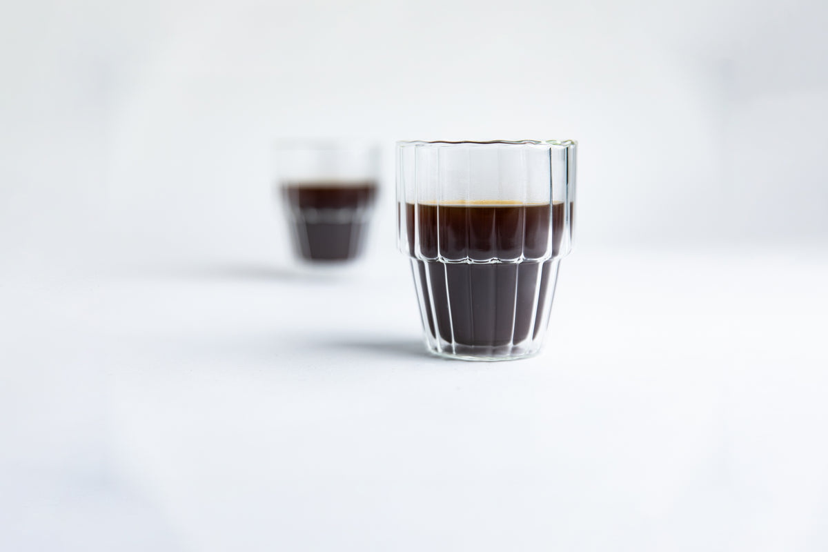 Two ribbed glass cups of dark liquid on a light gray background