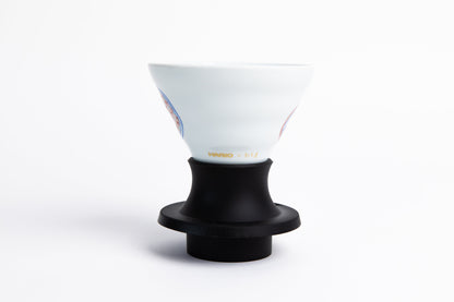 white cone-shaped coffee dripper with design in a black silicone base with clear plastic push switch. set on a white background