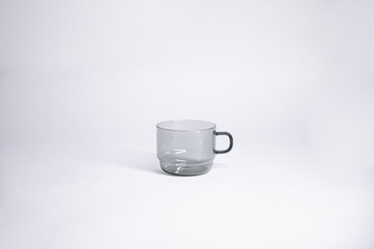 Small transparent gray glass mug with handle. set on white background