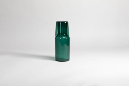 Transparent green carafe with matching glass cup flipped upside down on carafe top of carafe. Set on a light gray background