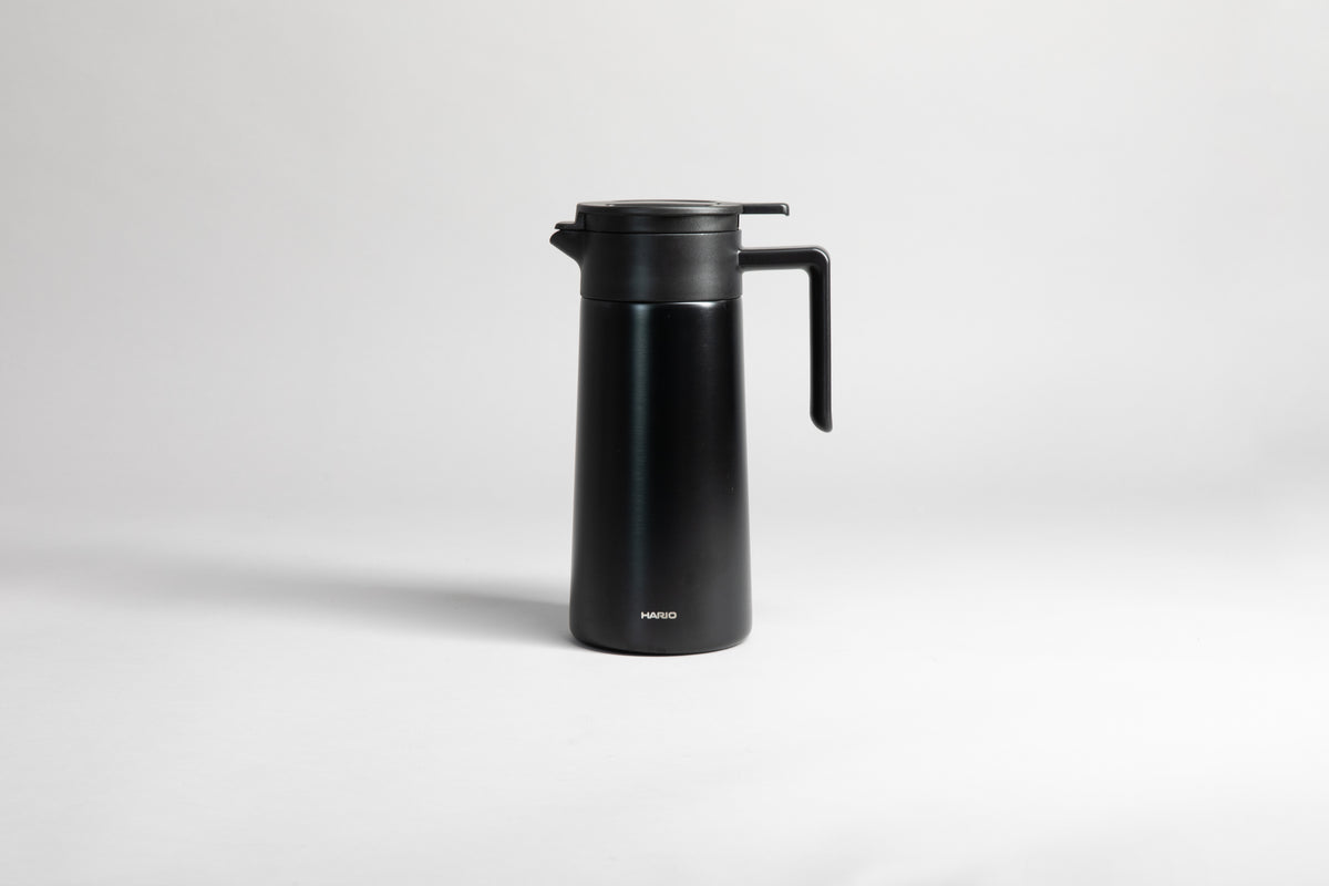 Black cylindrical pot with an black polypropylene spout, handle and lid. Set on a light gray background