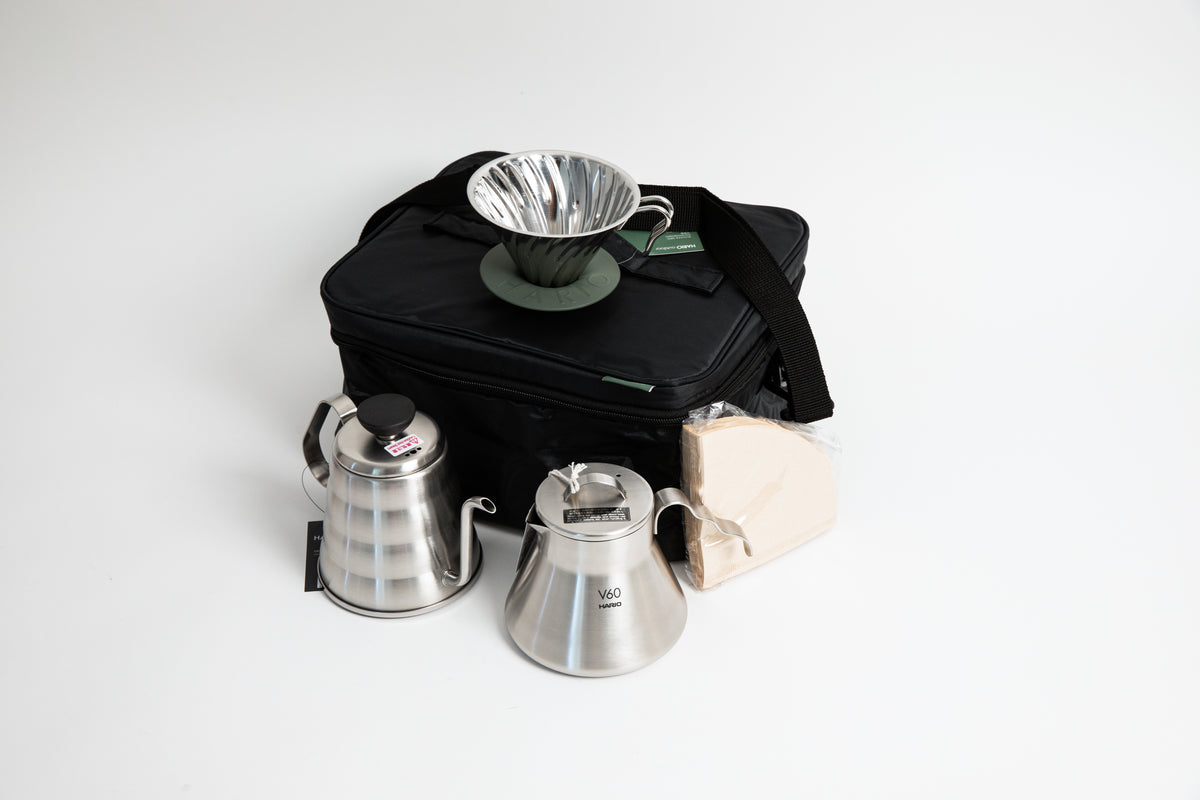 stainless steel kettle, metal cone coffee dripper with a olive green base stainless steel coffee sever pot, stainless steel lid and coffee filters with a black bag. on a white background. 