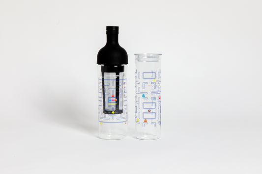 Tall glass container and black nylon mesh coffee filter, with black rubber wine bottle shaped top. Glass decorated with "pac-man" blue maze game with colorful ghosts and an yellow, circular figure with a wedge-shaped mouth.