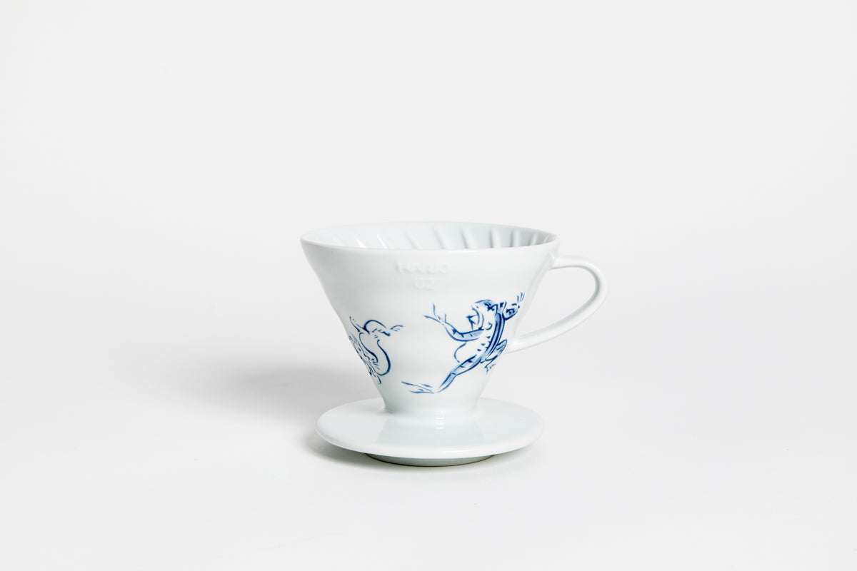 White cone-shaped ceramic coffee dripper with handle and round base, featuring The Chōjū-Giga V60 design in blue color, depicting the famous scene of a frog and rabbit wrestling, as well as a rabbit chasing a thief with a long stick. set on a white background.