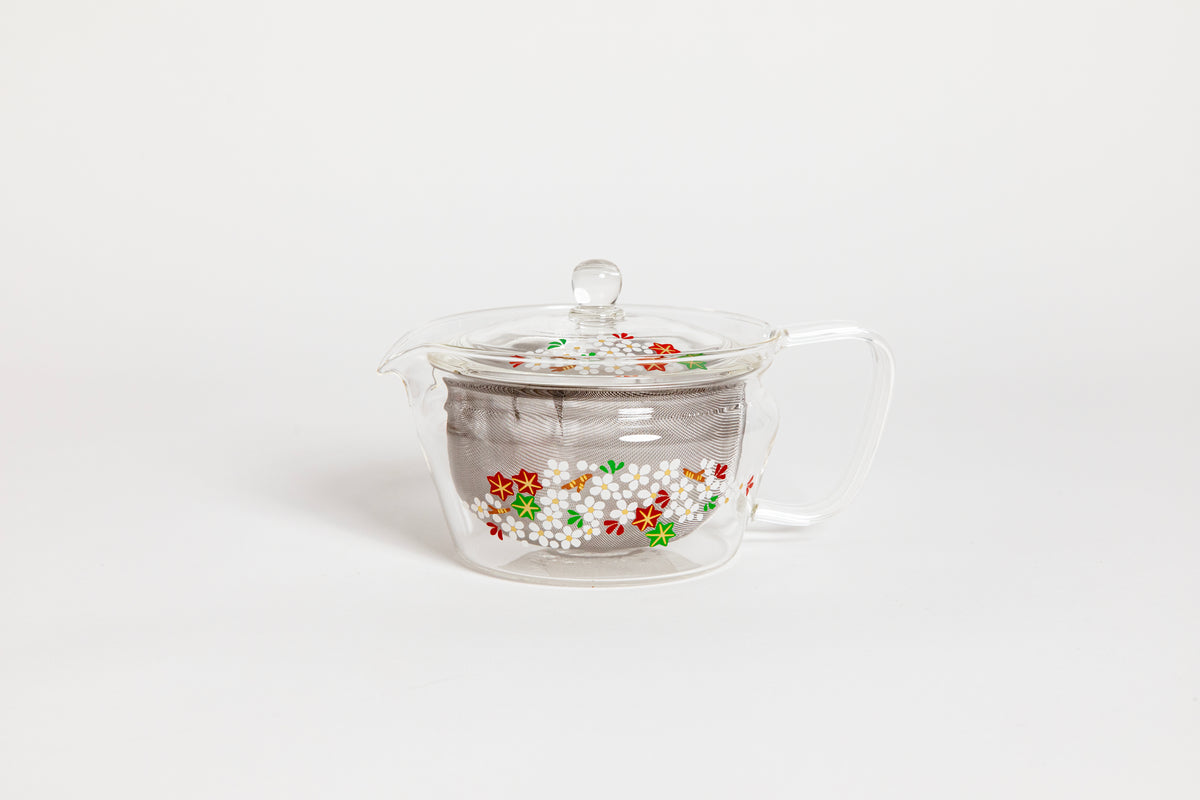 All glass tapered tea pot with flat bottom, all glass lid and handle, and metal mesh filter basket insert. Decorated with a yellow and white painting of "Cloud Nishiki", a cloud-like cherry blossoms colored in  white, red, green and beautiful brocade-like autumn leaves. Set on white background