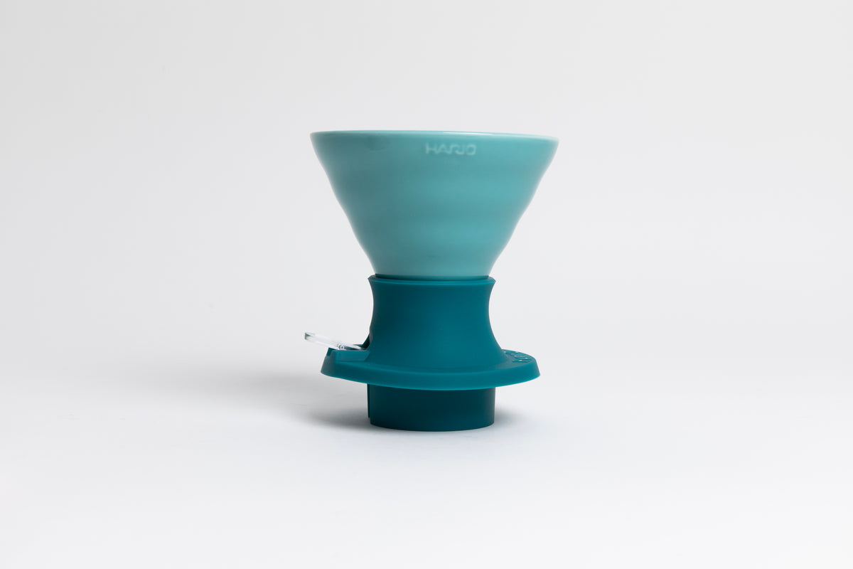 Cone-shaped turquoise ceramic dripper seated in a dark turquoise silicone base with clear plastic push switch on a white background.