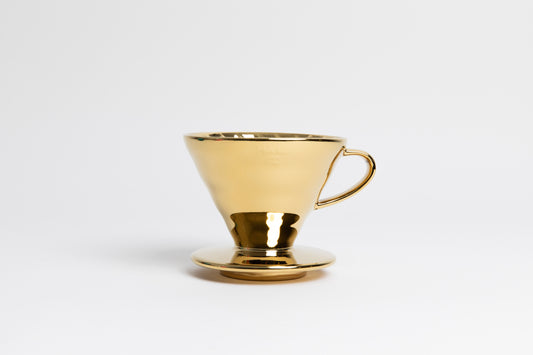 Metallic gold cone shaped ceramic coffee dripper with handle and round base. Set on white background