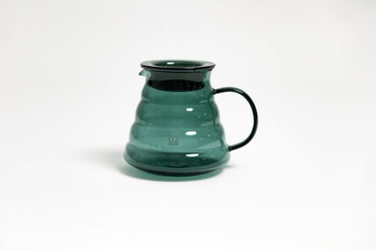 All glass transparent dark green beehive shaped coffee server with glass handle and glass lid with dark plastic rubber gasket on white backdrop.