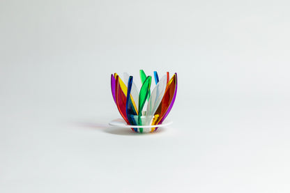 Transparent rainbow in the colors red, blue, green, white, orange, purple and yellow pedals in a spiral shape on a transparent black base on a white background.