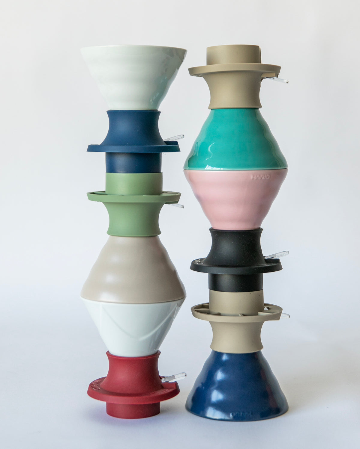 A colorful assortment of V60 ceramic cone coffee drippers with various silicone  bases, arranged in a stack on a white background. 