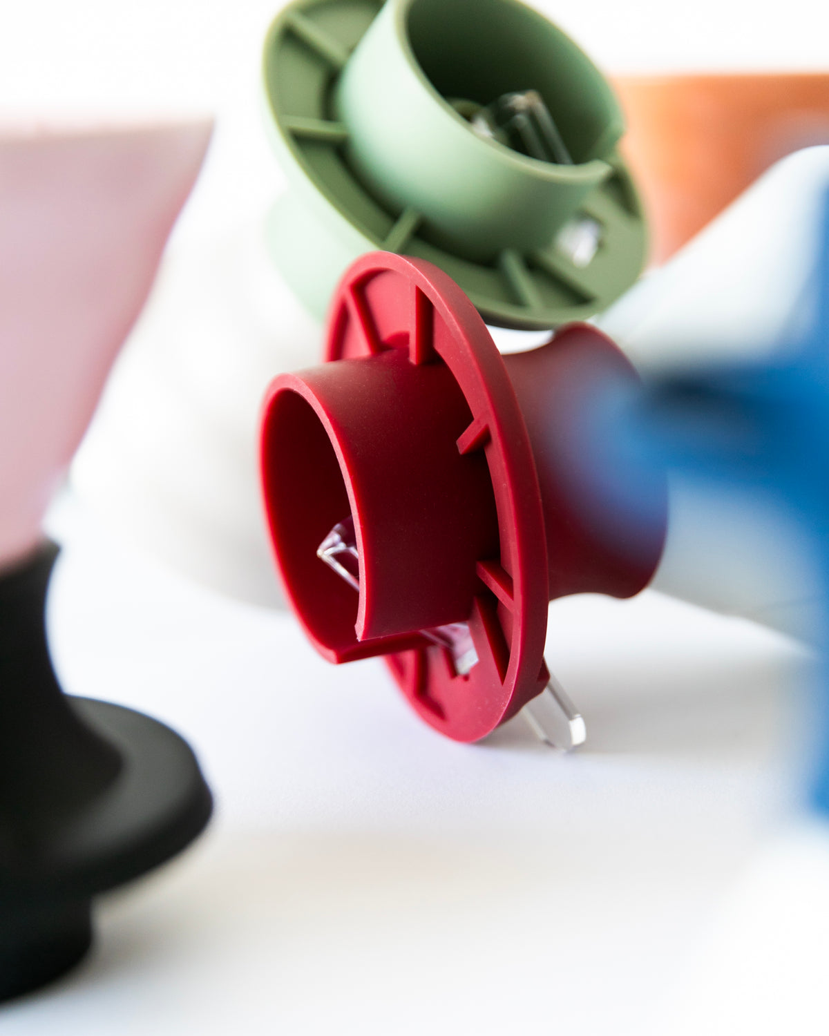 Close up of colorful silicone coffee maker inserts with cylindrical and flared shapes, with clear tab button in the color red and green on a white background