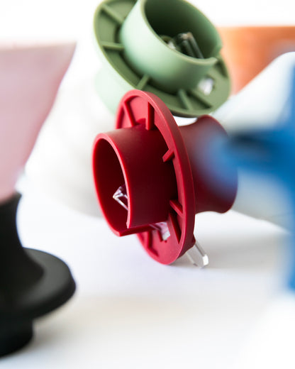 Close up of colorful silicone coffee maker inserts with cylindrical and flared shapes, with clear tab button in the color red and green on a white background