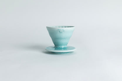 A ceramic pour-over cone with a saucer base featuring a gradient crackle glaze from light teal to teal. The text 'HARIO 01' is displayed on the cone. Set against a light gray background.