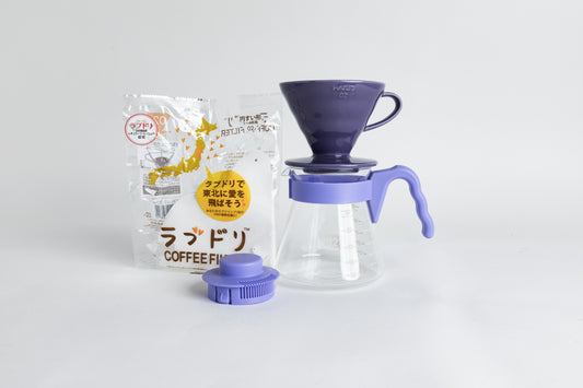 Purple HARIO 02 cone dripper on a glass carafe with a purple handle, shown with paper filters and a matching purple lid on a light gray background.