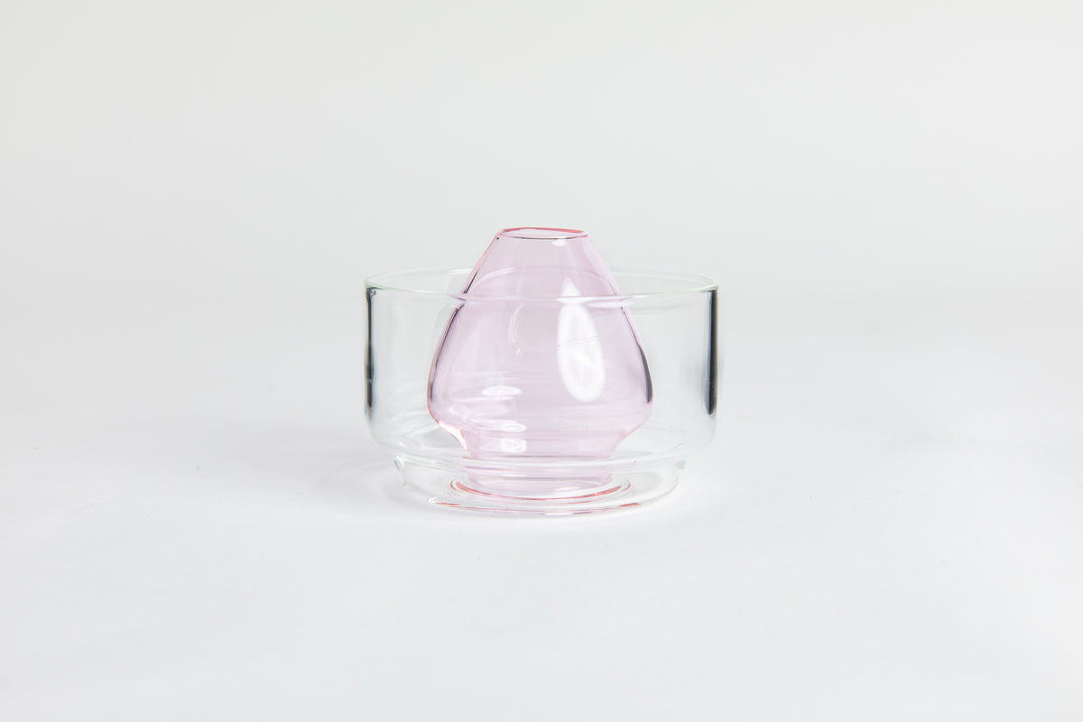 Dome-shaped pink clear glass matcha whisk holder with a smooth, tapered form, placed inside a clear glass base. Displayed on a white background with 'Hario' branding
