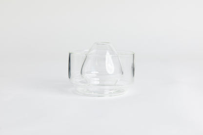 Dome-shaped clear glass matcha whisk holder with a smooth, tapered form, placed inside a clear glass base. Displayed on a white background with 'Hario' branding