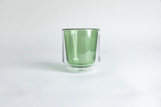 A clear double-walled glass with green colored interior cup. set on a white background
