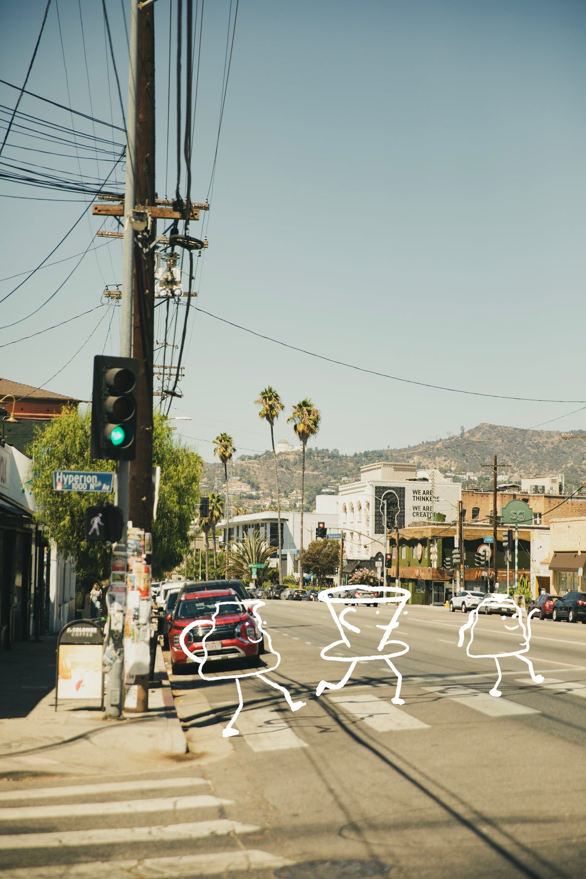 Street scene with hand drawn characters walking, traffic lights, power lines, and a clear sky.