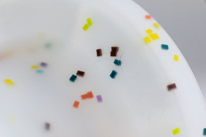 close up on the speckles on the white base. speckles are in the color: orange, purple, dark teal, yellow and lime green.