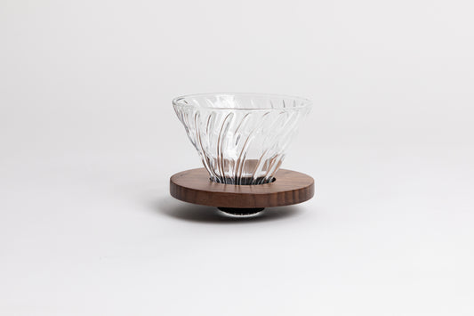 Clear all glass cone shaped coffee dripper with ribs, sitting in a round walnut wood base.