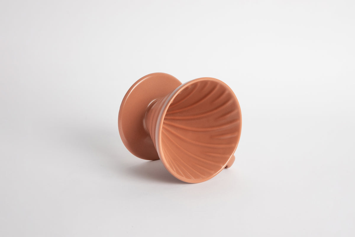 Burnt Orange colored 60 degree cone shaped ceramic coffee dripper with handle and round base. Spiral ribbed on the inside cone. Set on white background