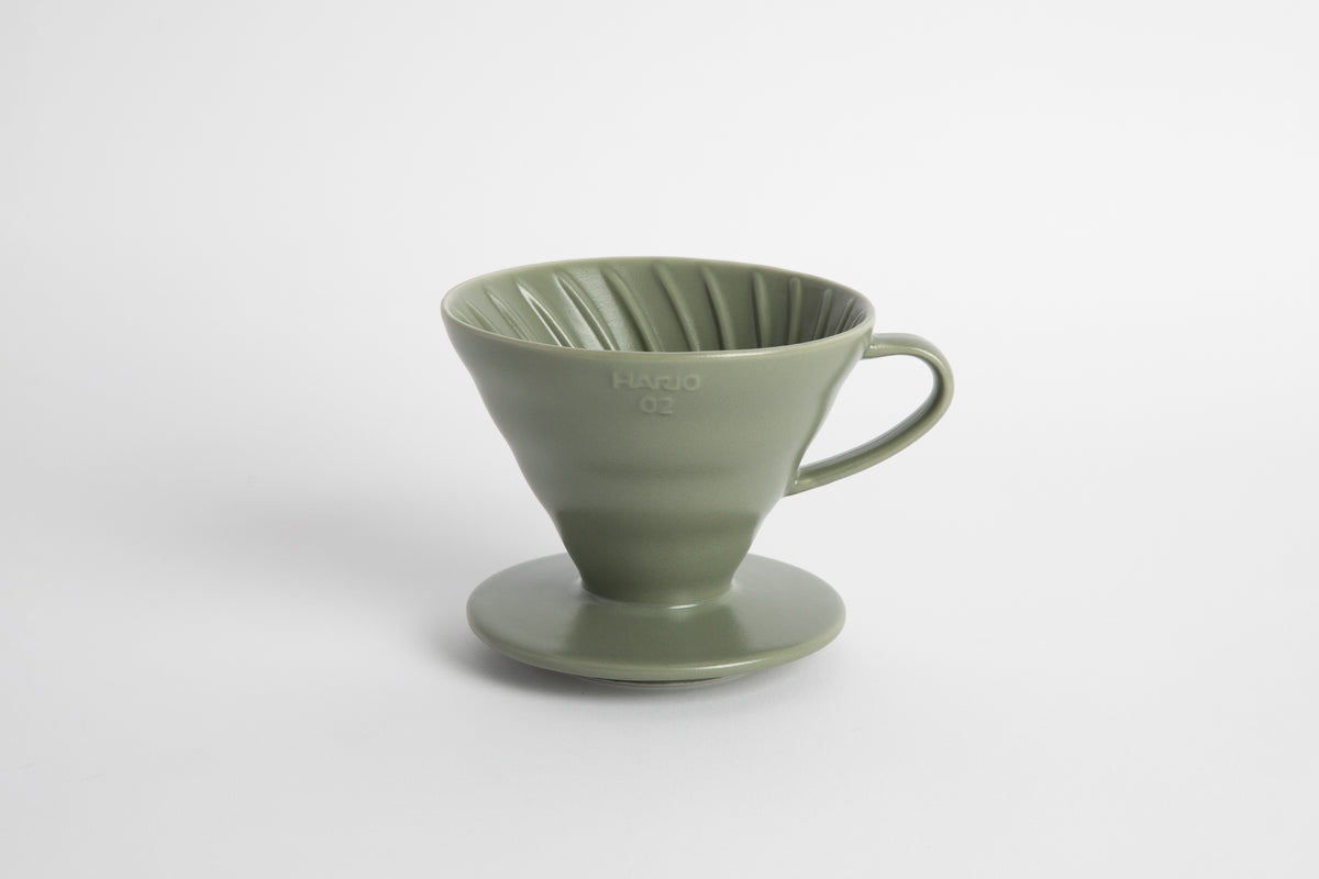 "Oil Green" sage colored 60 degree cone shaped ceramic coffee dripper with handle and round base. Spiral ribbed on the inside cone. Set on white background