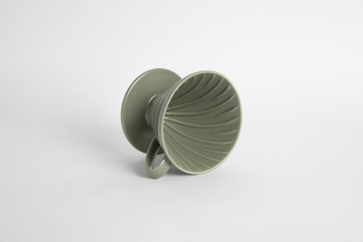 "Oil Green" sage colored 60 degree cone shaped ceramic coffee dripper with handle and round base. Spiral ribbed on the inside cone. Set on white background