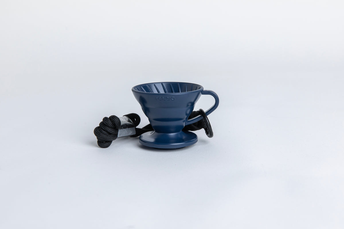 navy blue cone shaped plastic coffee dripper  cup with handle and round base.  with a black rope tied on the handle Set on white background