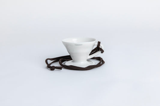 white cone shaped ceramic coffee dripper  cup with handle and round base.  with a brown rope tied on the handle Set on white background
