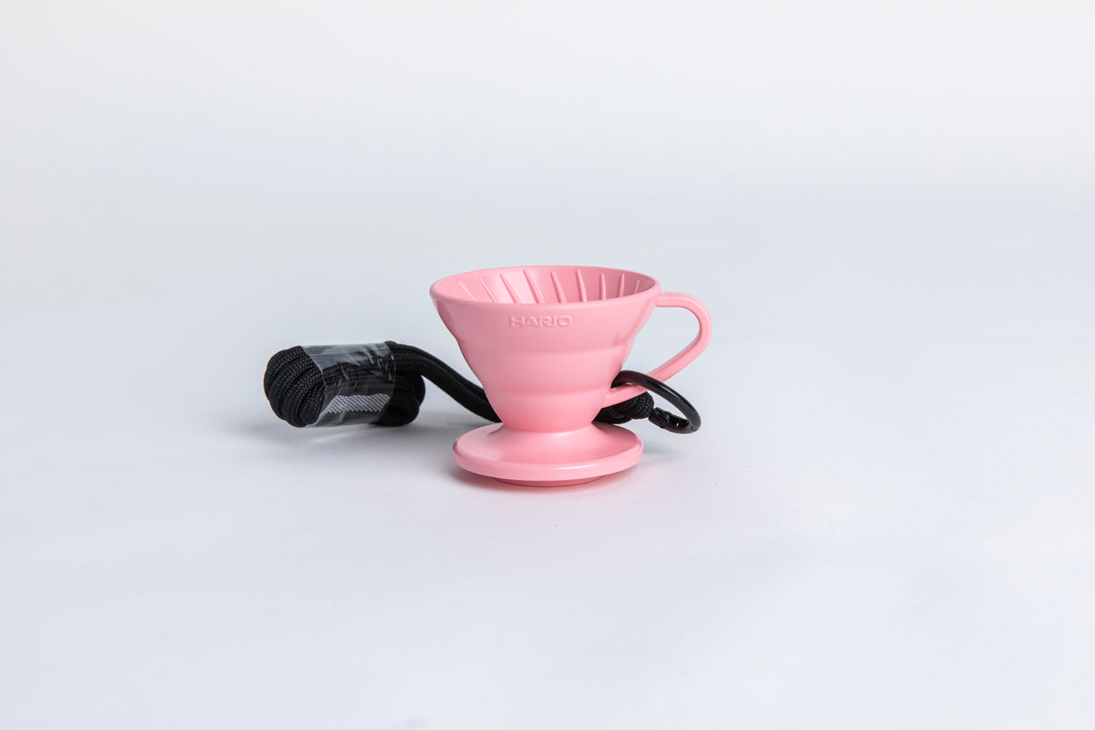 pink cone shaped plastic coffee dripper  cup with handle and round base.  with a black rope tied on the handle Set on white background