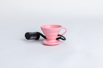 pink cone shaped plastic coffee dripper  cup with handle and round base.  with a black rope tied on the handle Set on white background