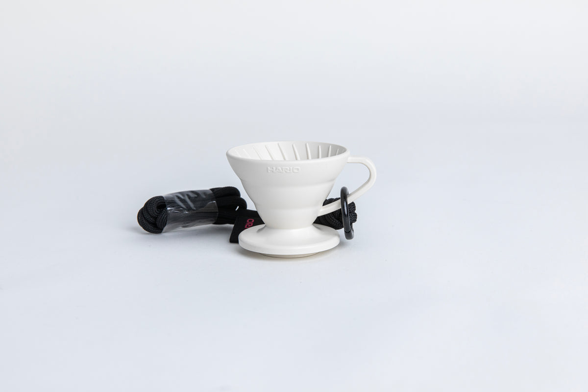 white cone shaped plastic coffee dripper  cup with handle and round base.  with a black rope tied on the handle Set on white background