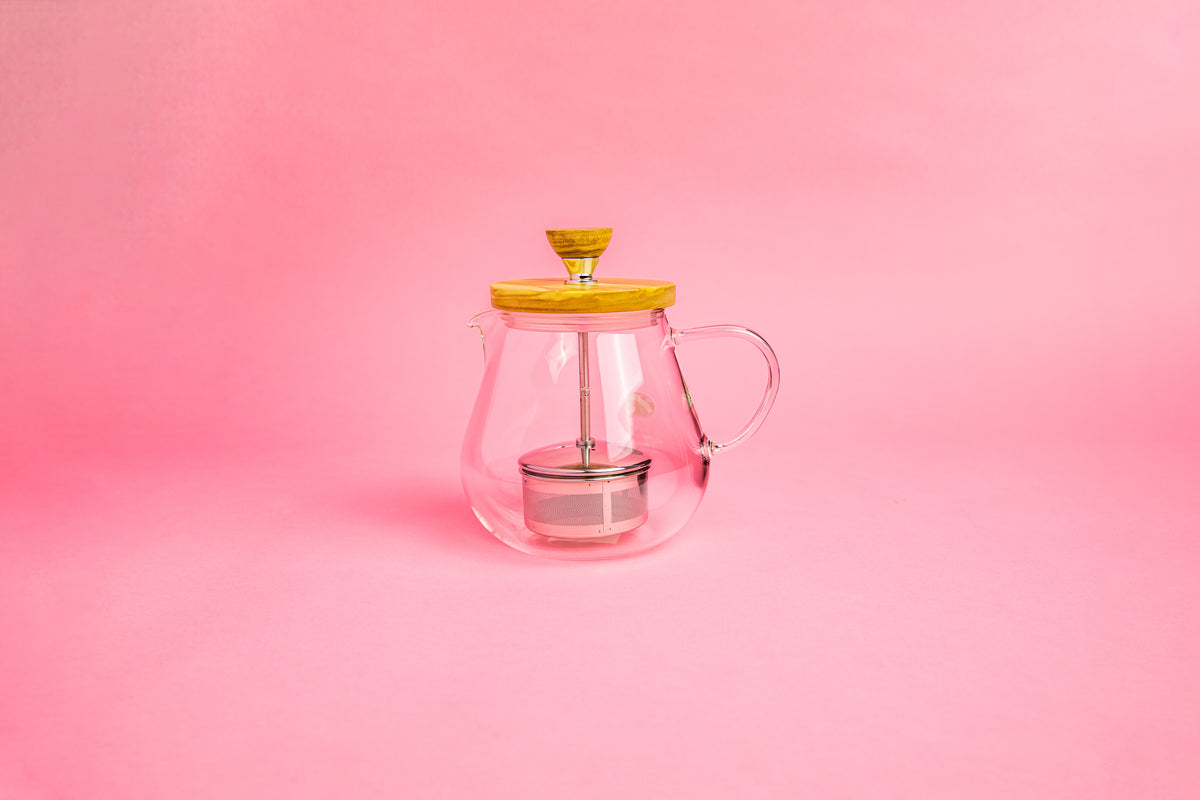 Glass teapot with glass handle. Olive wood lid and knob. Stainless steel plunger with metal tea filter basket . set on pink gradient background